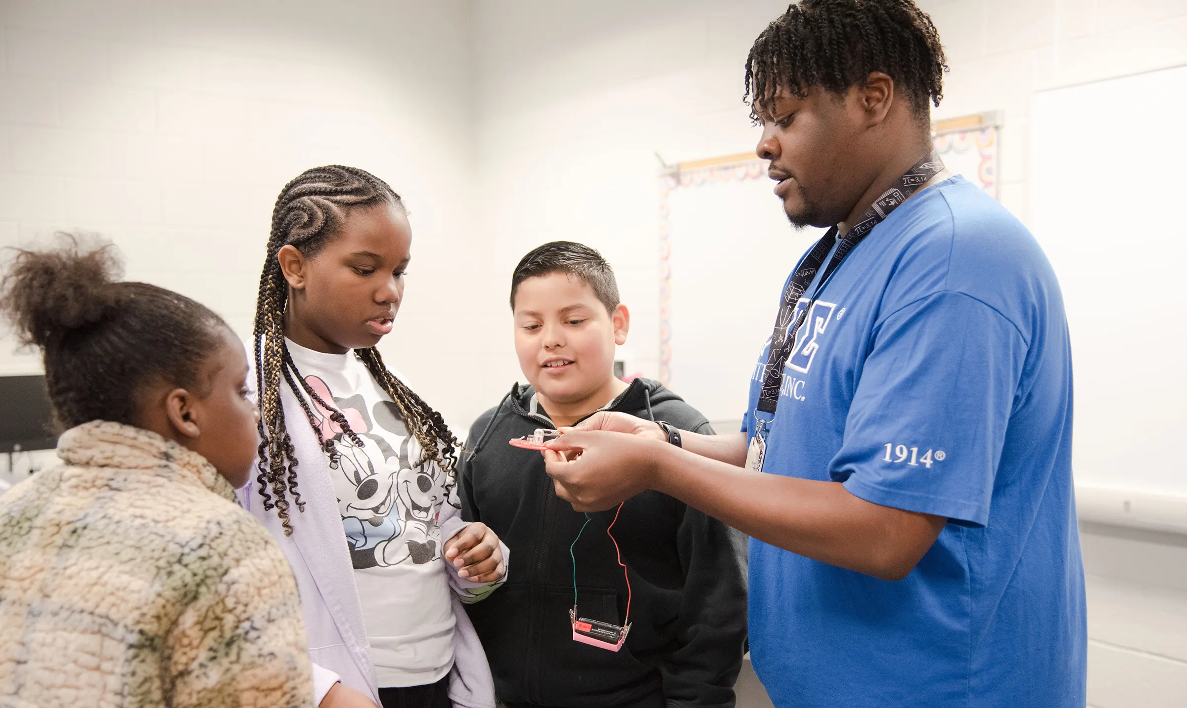 a teacher with 3 students looking at a battery powered experiment