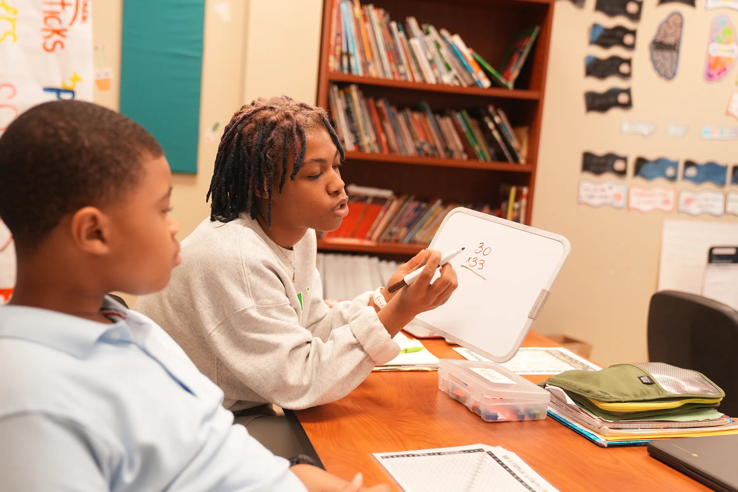 a teacher and student sitting a one desk working on a math problem on a whiteboard