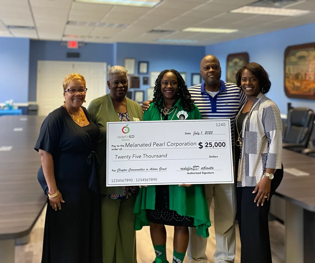 Group of 5 adults gathered around a giant check made out to Melanated Pearl for $25,000