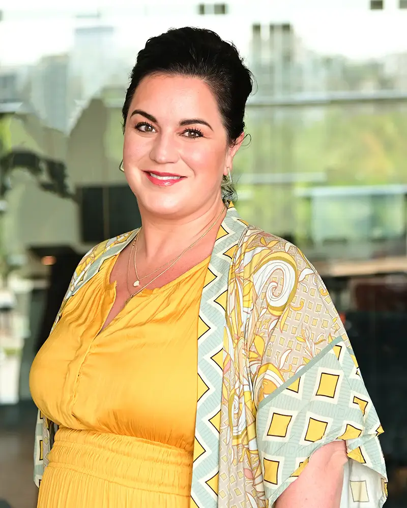 Emily with hair pulled back, wearing a bright yellow dress and smiling at camera