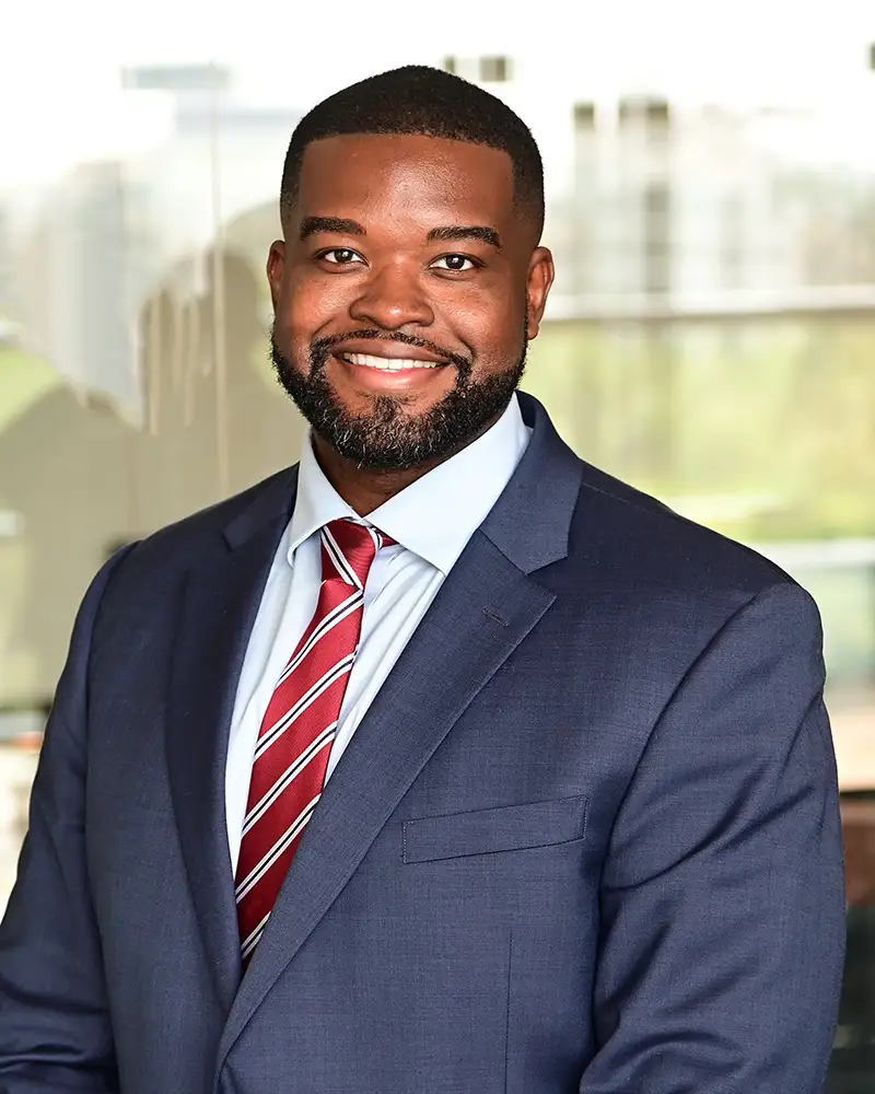 Lawrence in suit and tie, smiling at camera, blurred cityscape behind