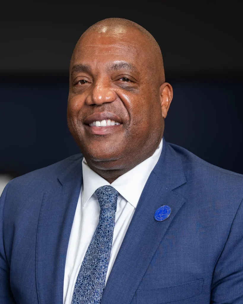 Keith in a blue suit, white shirt and tie, smiles at camera
